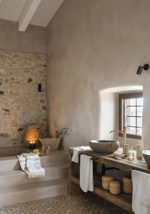rustic bathroom with stone wall, round washbasin, wooden furniture and golden tap.